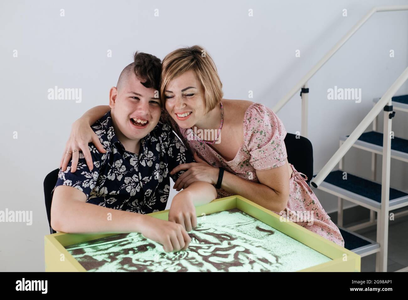 Children with disability getting sensory activity Sand tray, sand table for animation, cerebral palsy boy playing calming game, training fine motor Stock Photo