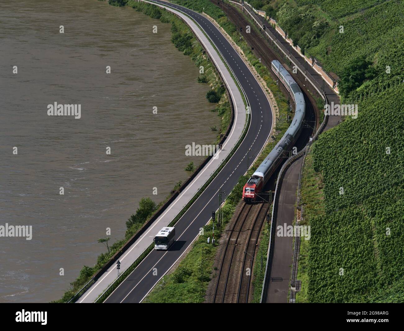 Aerial view of Rhine riverbank with InterCity (IC) passenger train, operated by Deutscha Bahn, passing a bus on the adjacent road on sunny summer day. Stock Photo