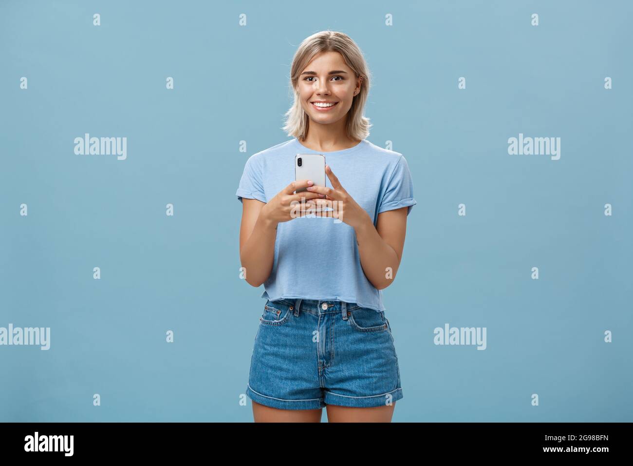 New phone is fantastic. Portrait of satisfied happy young modern blond woman in trendy outfit with blond short haircut smiling joyfull from delight Stock Photo