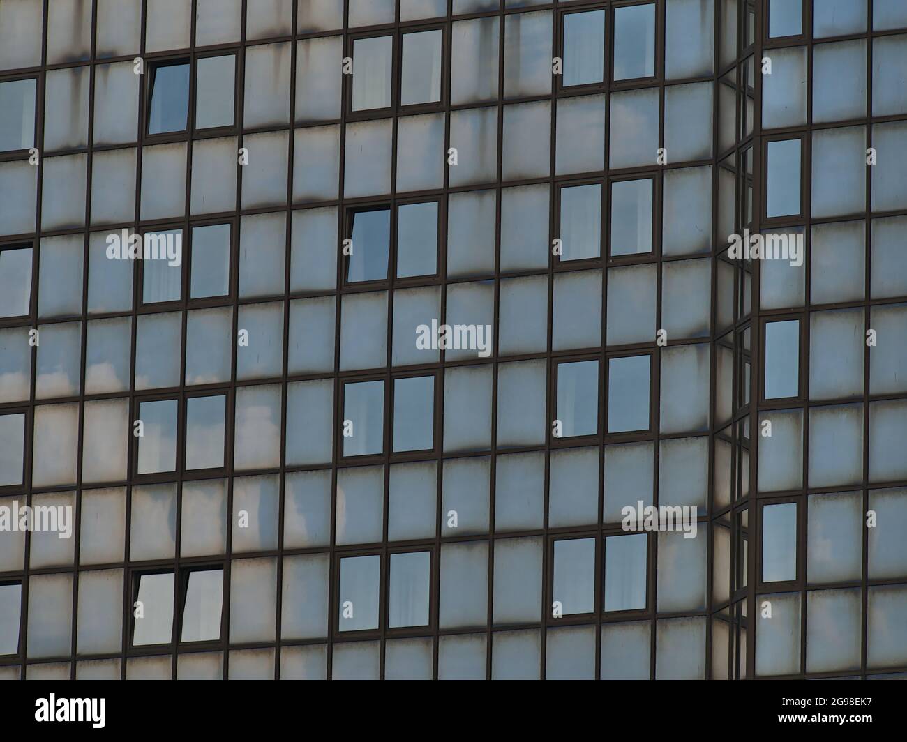 Closeup view of the facade of a commercial high-rise building with sky reflected in the dirty glass elements and opened windows. Stock Photo