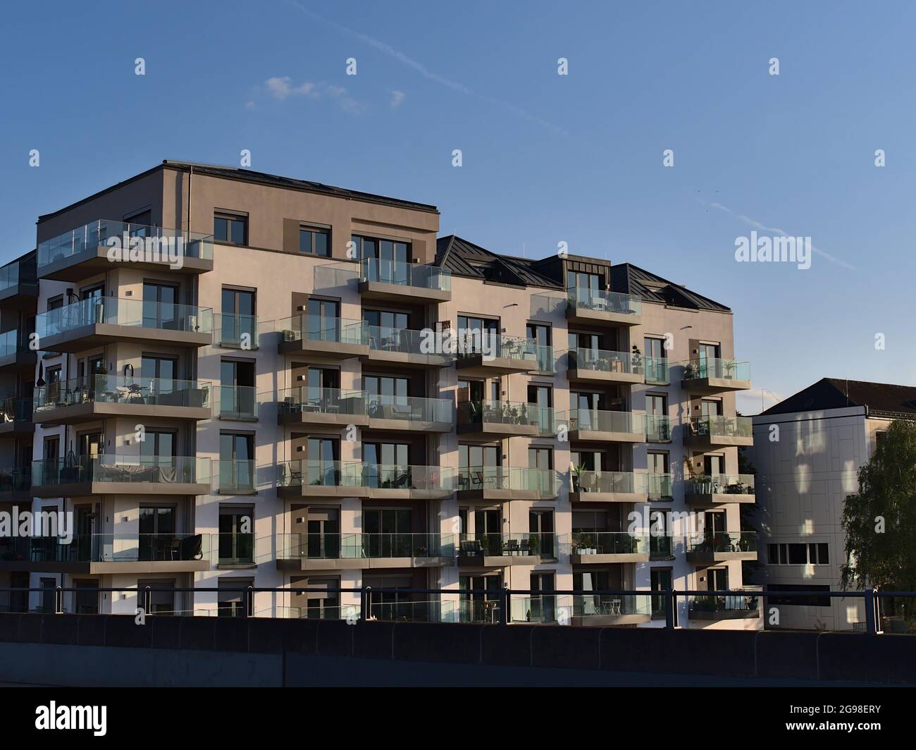 View of modern residential multi-family apartment building in luxury quality with balconies with glass railings in the evening sun with blue sky. Stock Photo