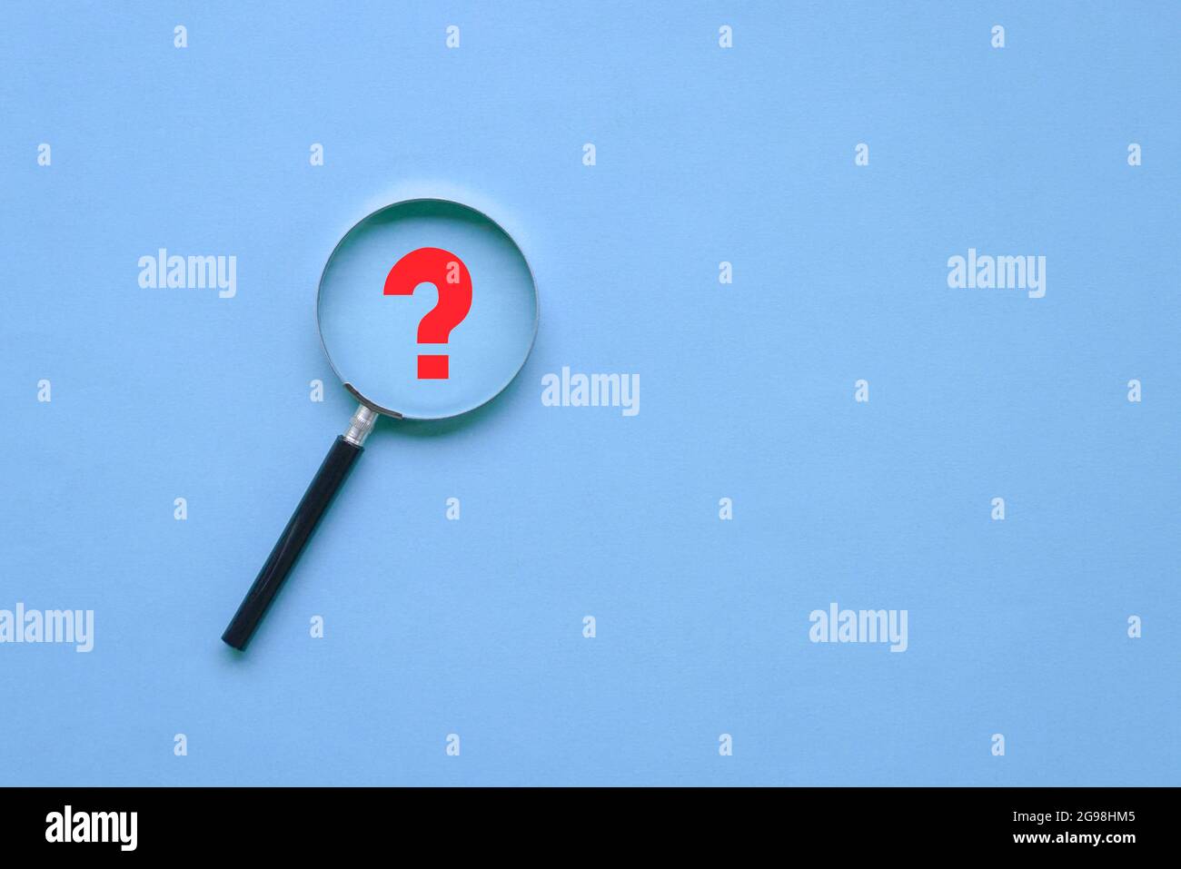 Magnifying glass and a red question mark on blue background. Copy space, top view. Stock Photo