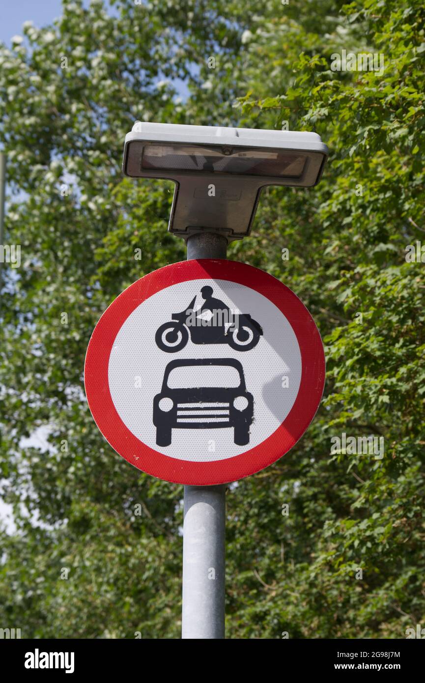 Circular road sign no motor bikes cars or motor vehicles allowed. Overhead light. against foliage UK Stock Photo