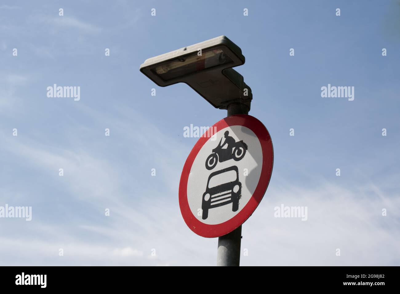 Circular road sign no motor bikes cars or motor vehicles allowed. against blue sky Overhead light. UK Stock Photo