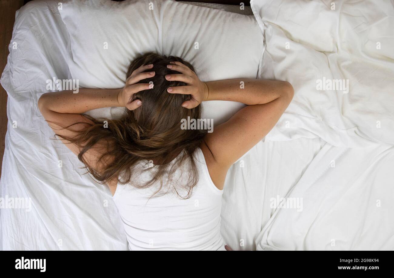 Young woman lying in bed suffering, tired woman covering face with