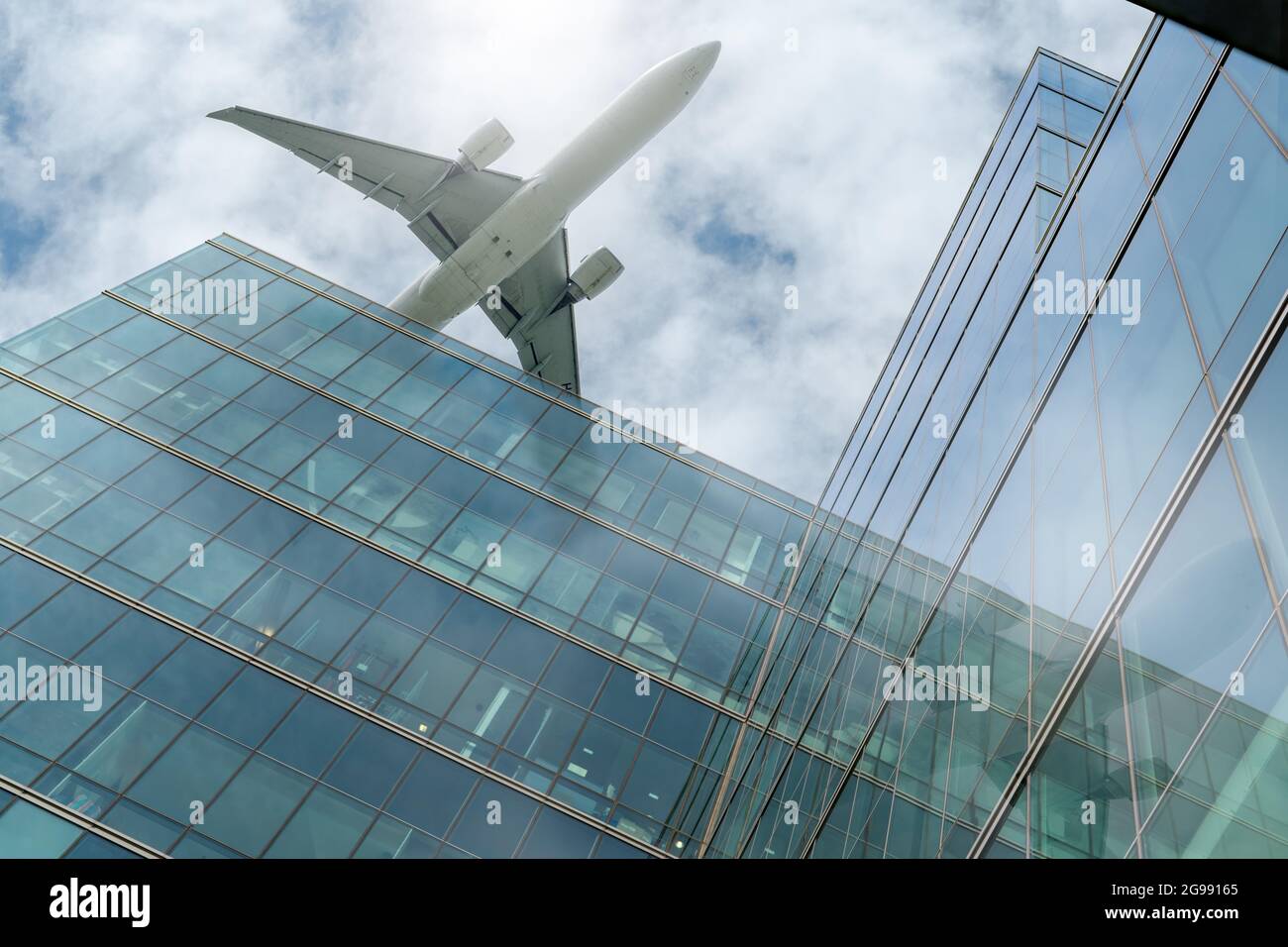 Airplane flying above modern office building. Exterior facade of skyscraper building. Business trip. Reflection in transparent glass windows. Aviation Stock Photo