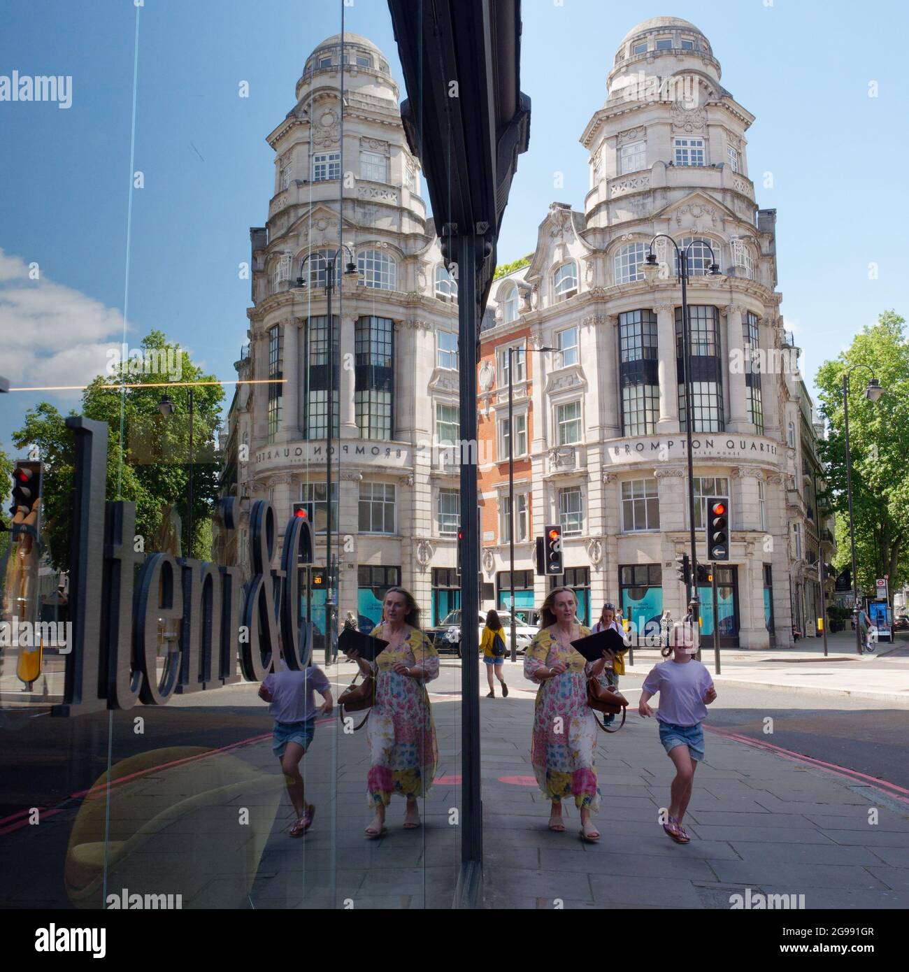 London, Greater London, England, June 12 2021: Mirror image reflection of Brompton Quarter Empire House with mother and  running in foreground. Stock Photo