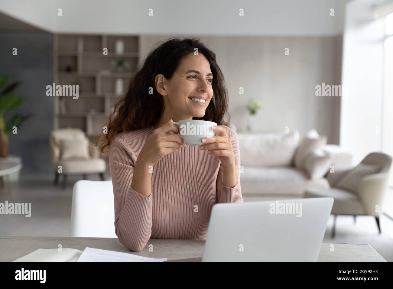 Smiling Latino woman drink coffee work on laptop Stock Photo