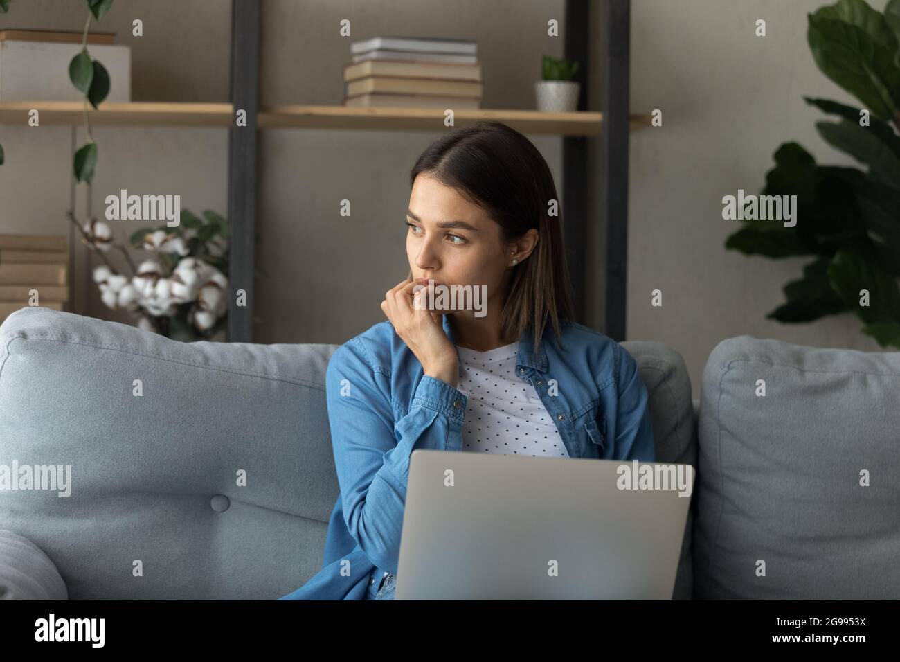 Pensive woman sit on sofa with laptop Stock Photo
