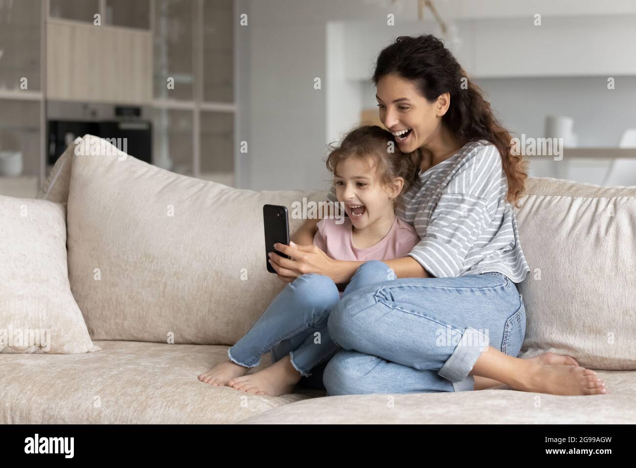 Excited Latino mom and daughter triumph using cellphone Stock Photo - Alamy