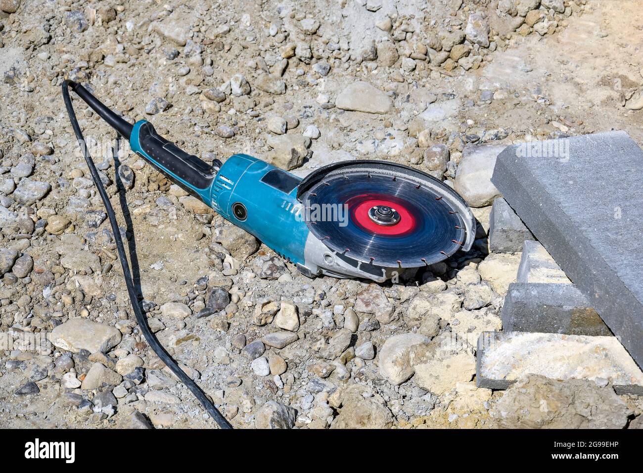 Electric tool with diamond disc for cutting stones lies on gravel. Angle grinder is ready for operation. Stone cutting technology. Close-up. Stock Photo