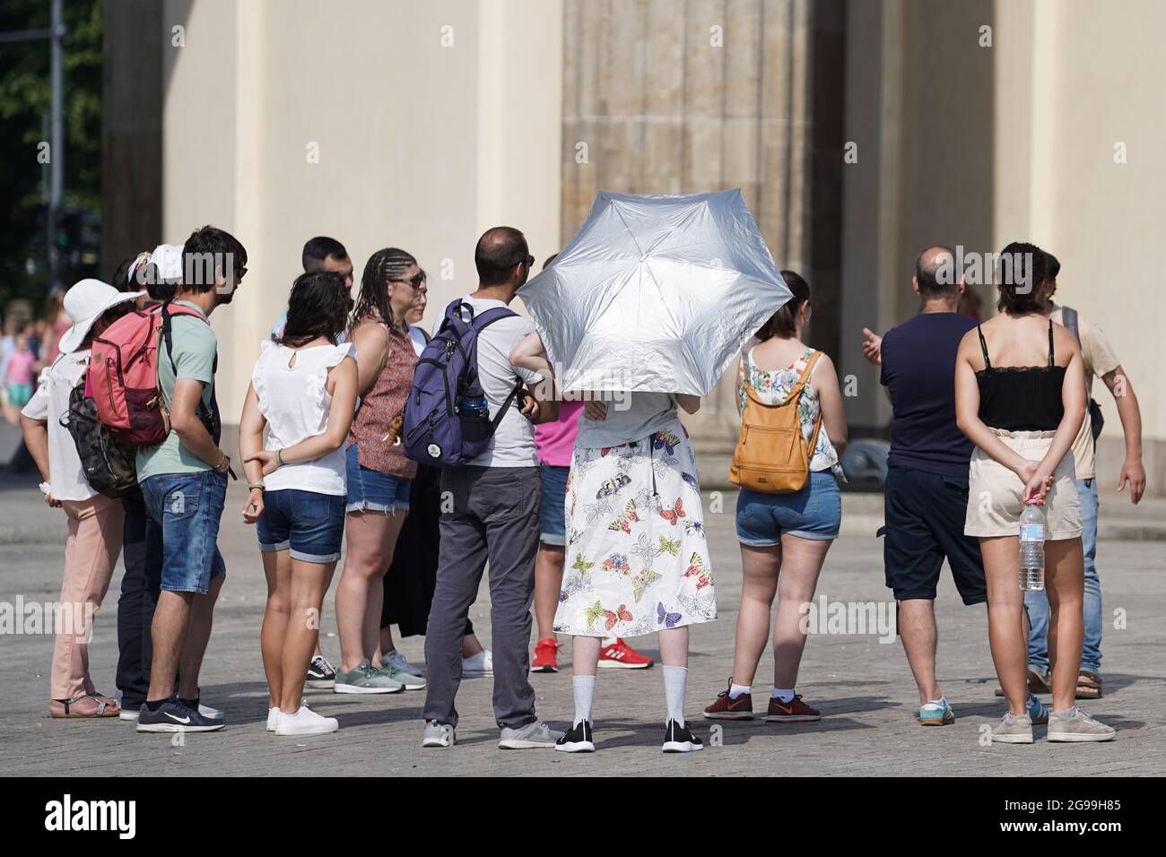 25 July 2021, Berlin: With a silver umbrella, the participant of a city tour protects herself from the rays of the sun in front of the Brandenburg Gate. Photo: Jörg Carstensen/dpa Stock Photo
