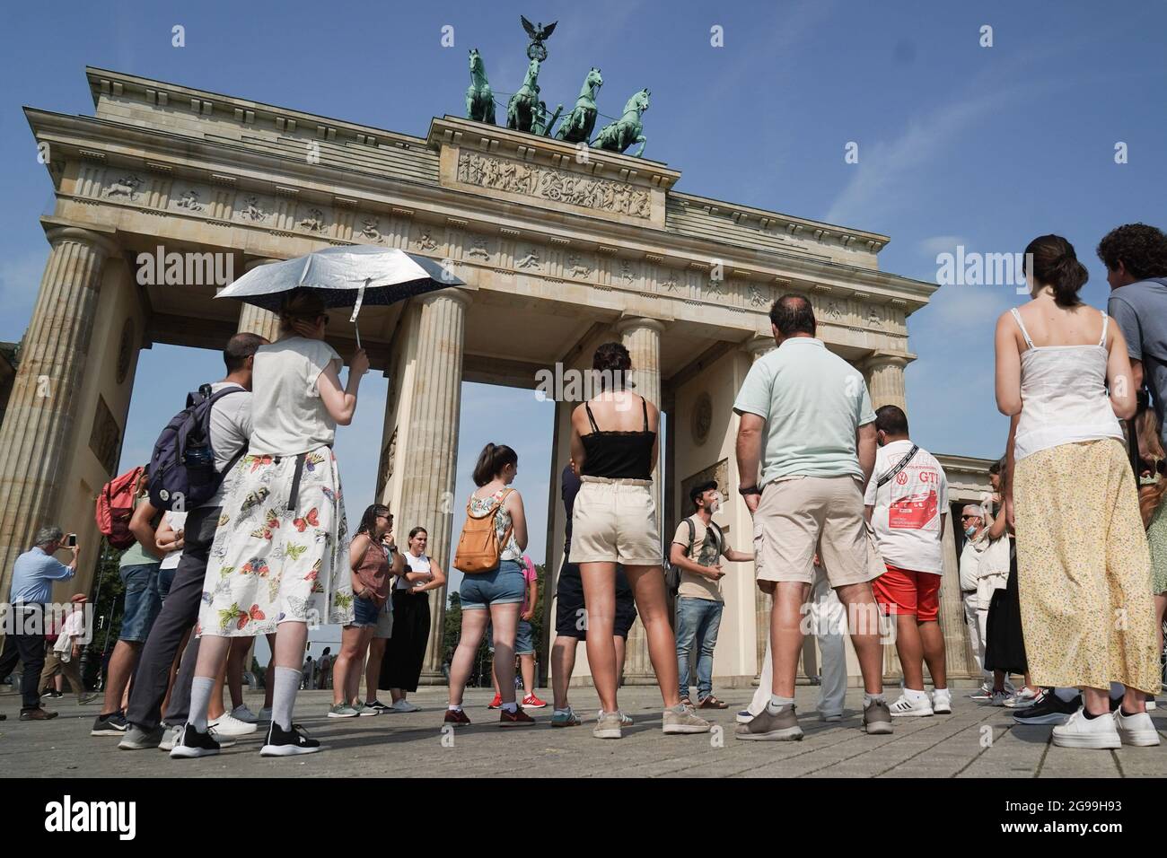25 July 2021, Berlin: With a silver umbrella, the participant of a city tour protects herself from the rays of the sun in front of the Brandenburg Gate. Photo: Jörg Carstensen/dpa Stock Photo