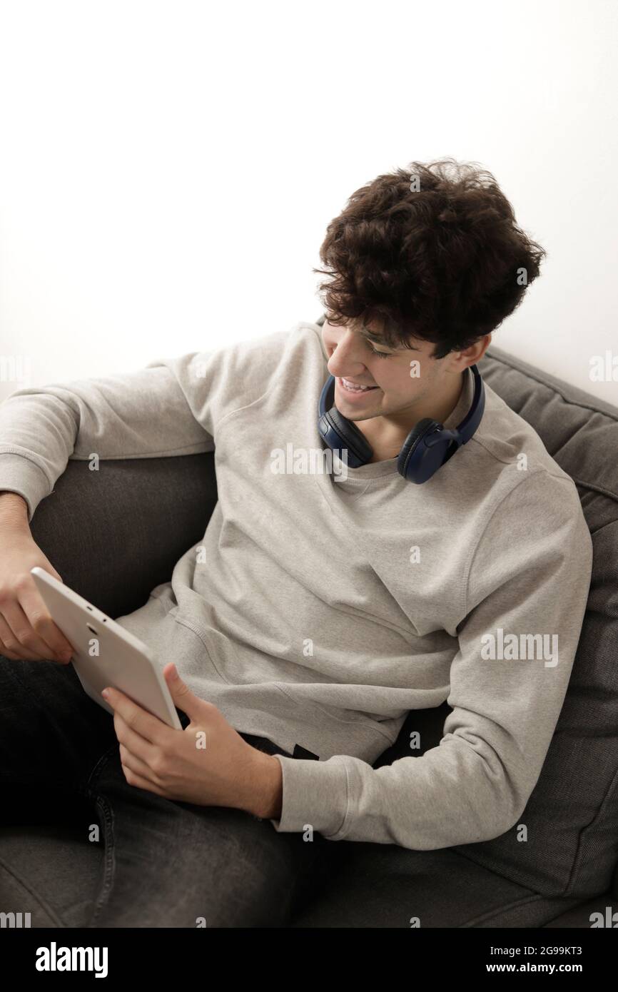 young man with headphones on his neck using his tablet in a sofa Stock Photo