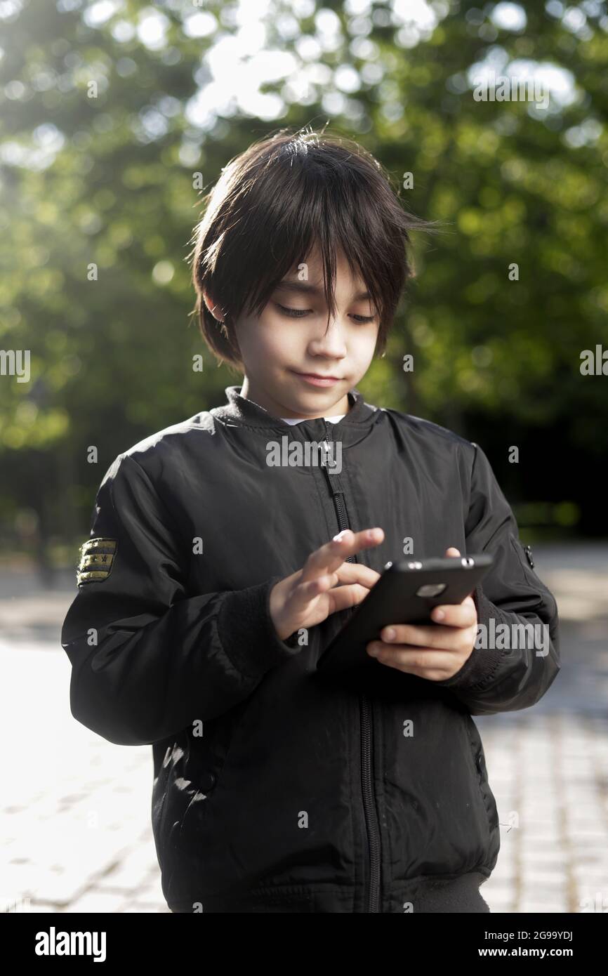 Hispanic toddler in a park playing with his cell phone. Hispanic boy holding the cell phone in the park Stock Photo