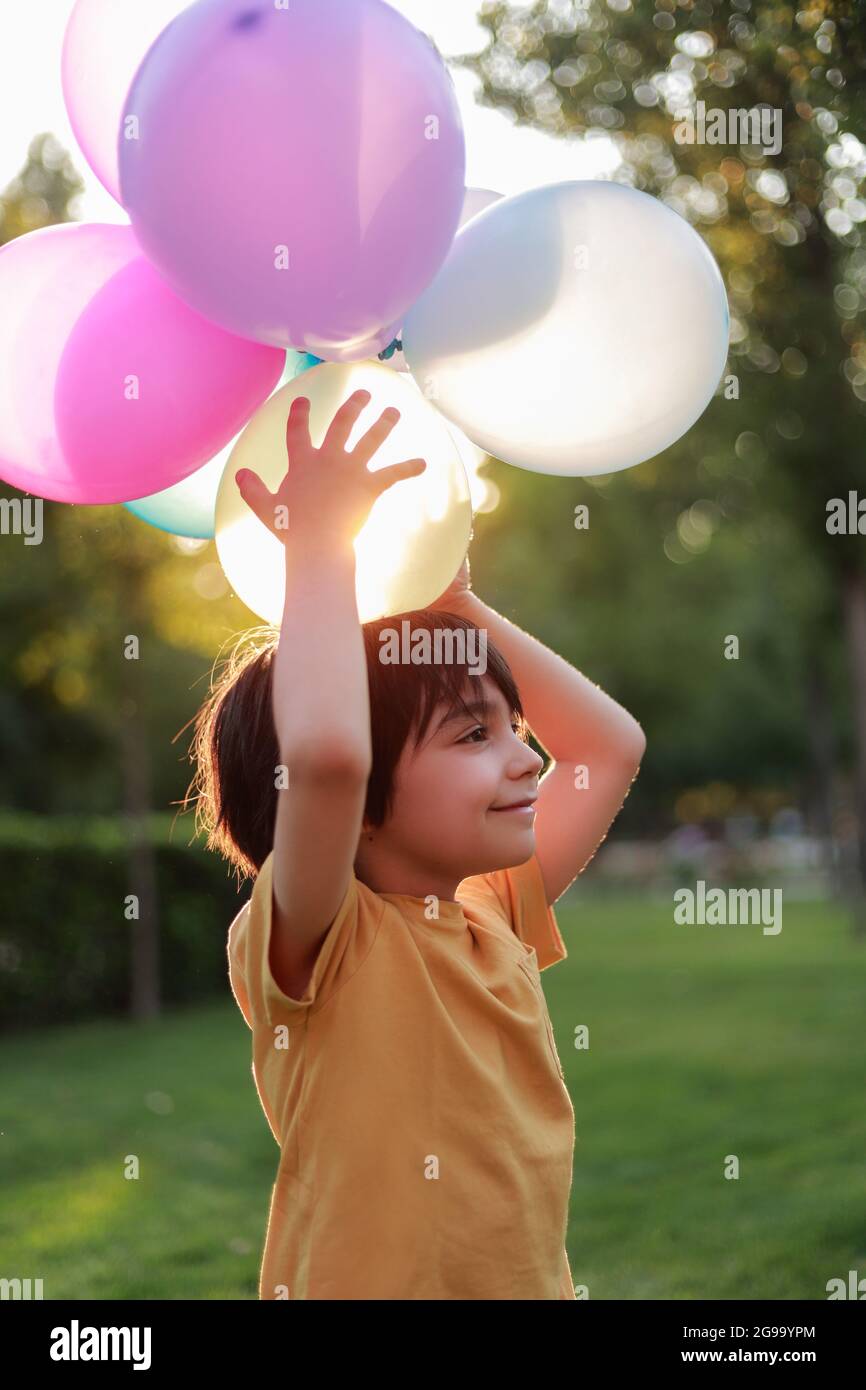 child in profile in the park playing colored balloons on his head and the sunset Stock Photo