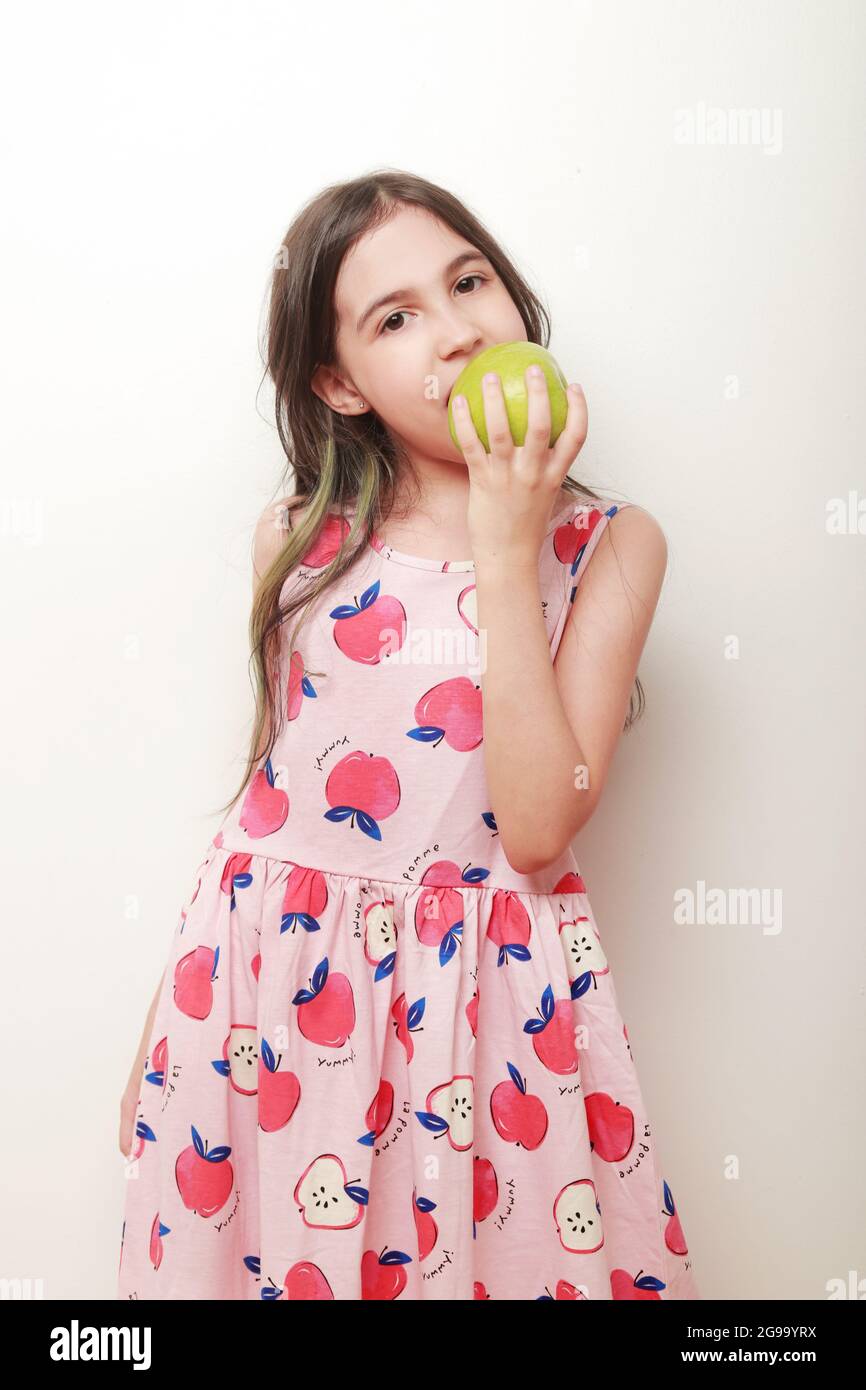 latin girl looks at camera with the action of eating a green apple and an apple print dress Stock Photo