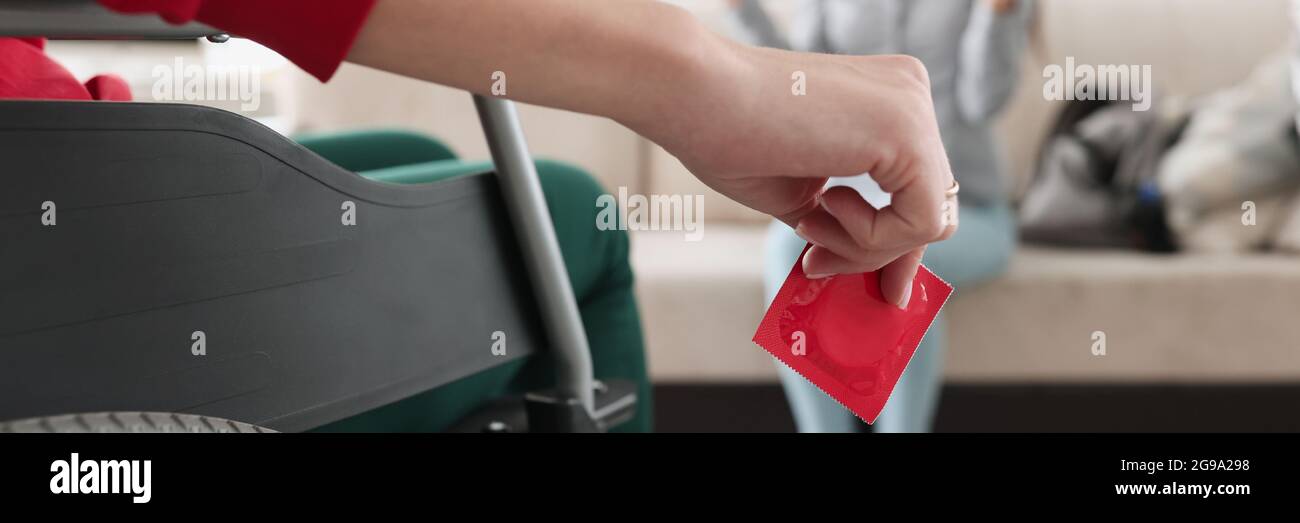 Person sitting in wheelchair holds red condom in his hand in front of woman sitting Stock Photo