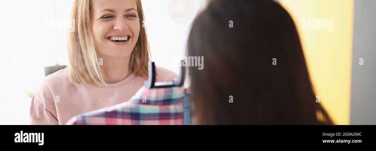 Smiling woman demonstrates clothes on hanger to client Stock Photo