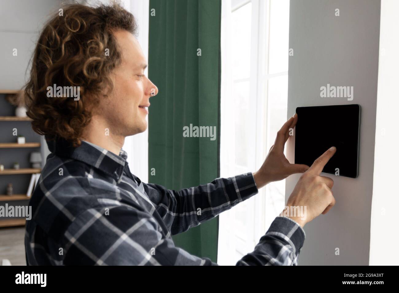 Man Using Tablet On Wall With Smart Home Application Indoors Stock Photo