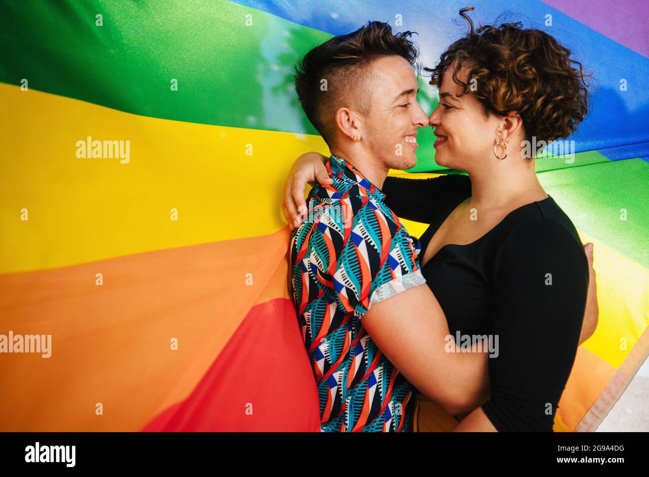 Romantic queer couple bonding against a rainbow pride flag. Young LGBTQ