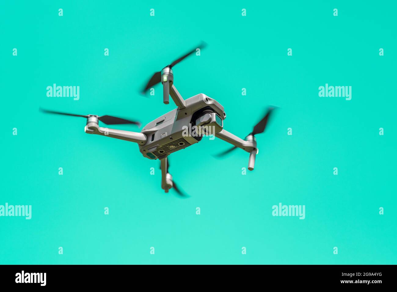 Flying drone with camera on turquoise background with copy space. Airborne quadcopter. Also known as a drone or UAV, Unmanned Aerial Vehicle. Low angl Stock Photo