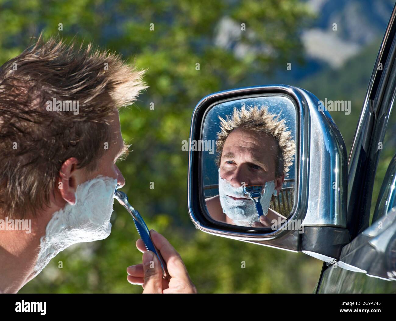 man shaving in the side mirror of his car on roadtrip Stock Photo