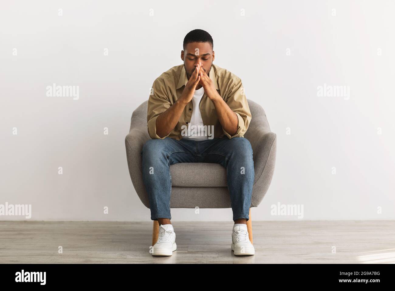 Frustrated African Guy Thinking About Problems Sitting Over Gray Wall Stock Photo