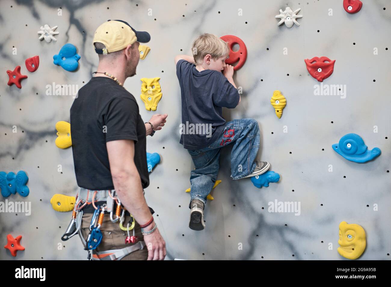 climbing coach assisting young boy on bouldering wall Stock Photo