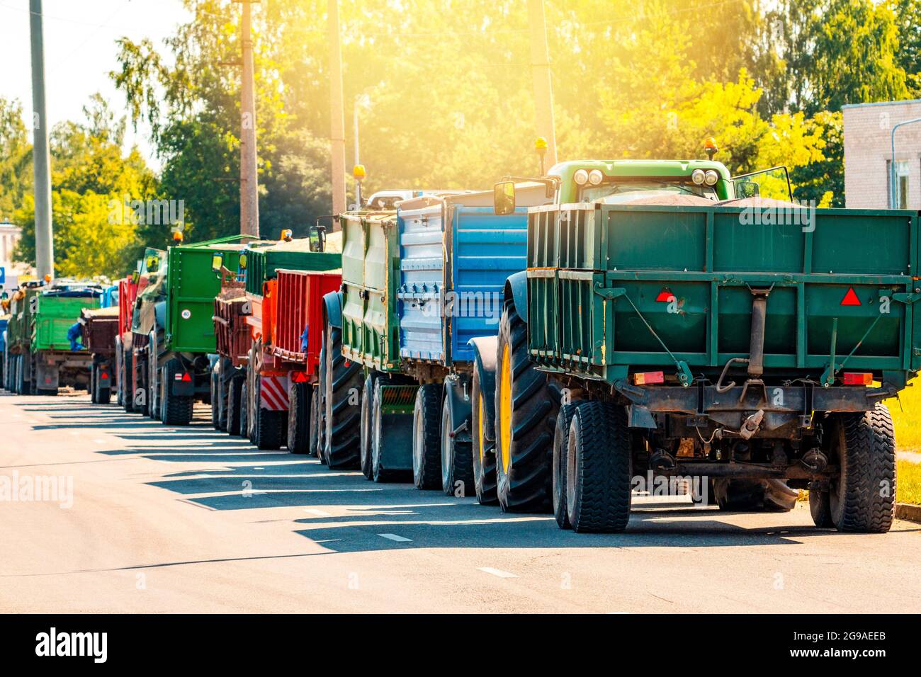 Tractors delivering recently harvested grain, stretching along the road Stock Photo