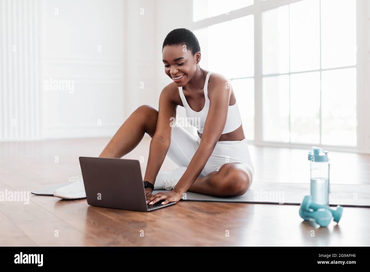 Smiling young black woman sitting on yoga mat using laptop Stock Photo ...