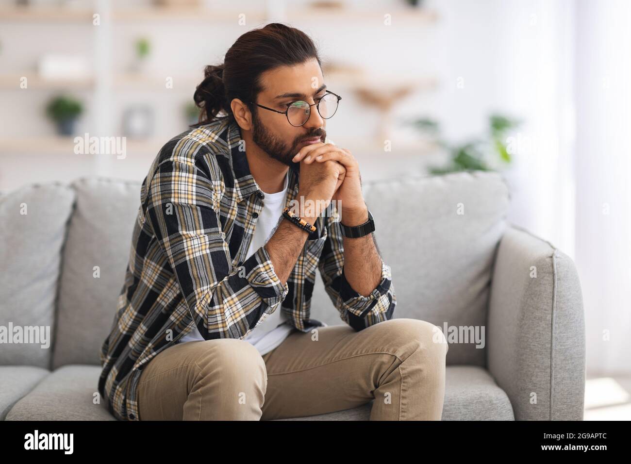 Pensive arab guy sitting on couch at home Stock Photo