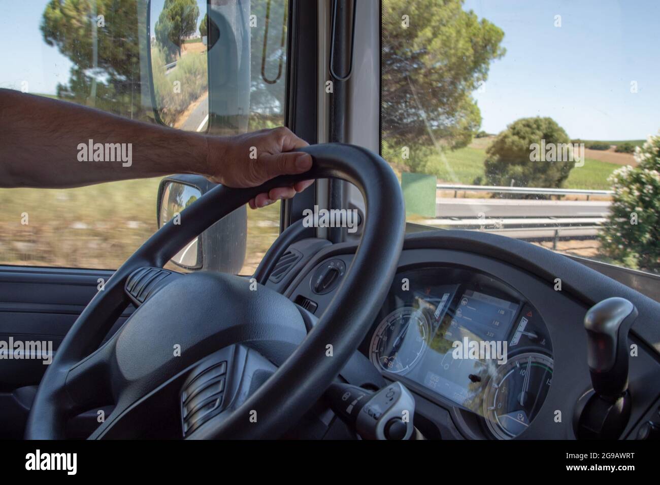 Dashboard and steering wheel of a truck with a driver's hand holding it while driving. Stock Photo