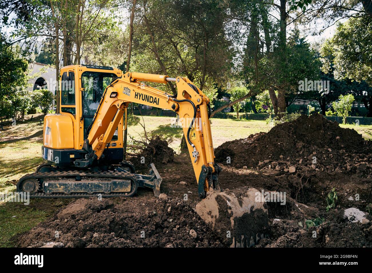 Yellow excavator digs the ground in a green park Stock Photo - Alamy