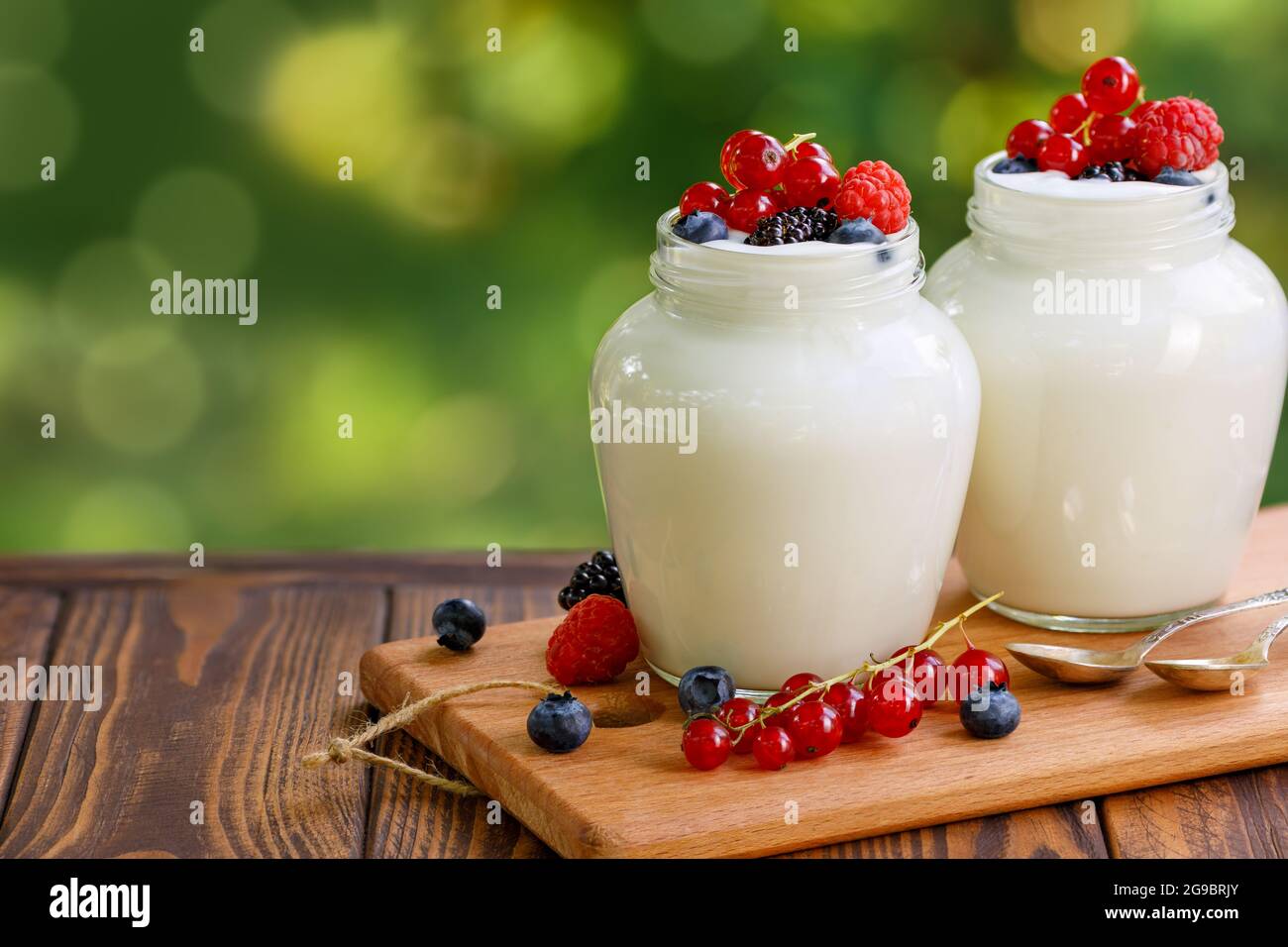 yogurt and fresh berries in two glass jars on table outdoors Stock Photo