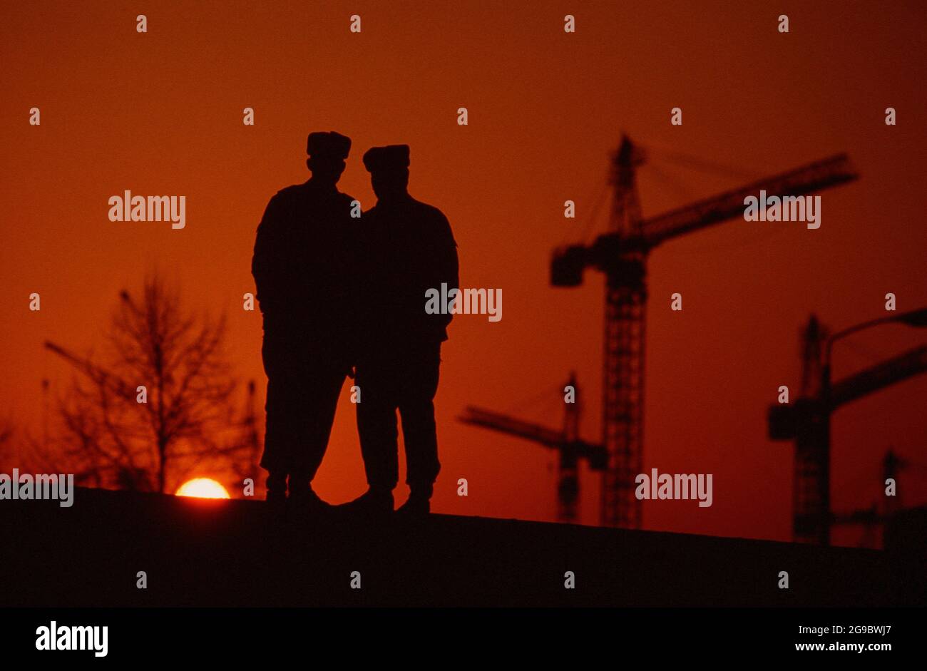 East German policemen stand atop a section of the Berlin Wall at sunset, circa 1980s Stock Photo