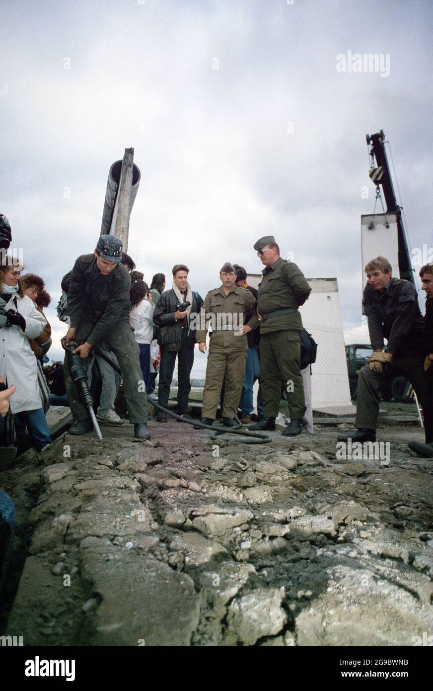 East German police and West German citizens watch as a workman ...