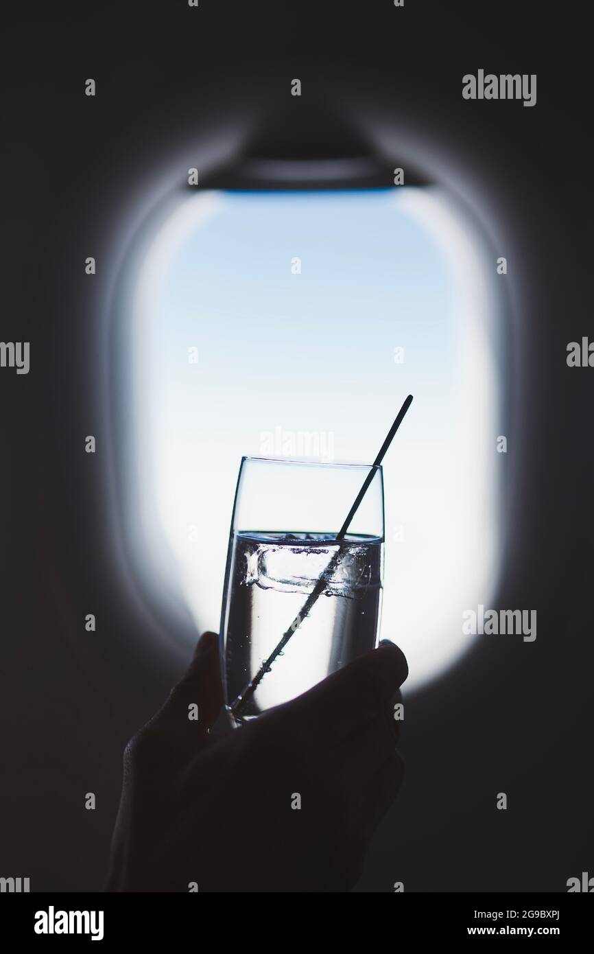 Passenger enjoy drink during flight. Man holding glass of gin and tonic against airplane window. Stock Photo