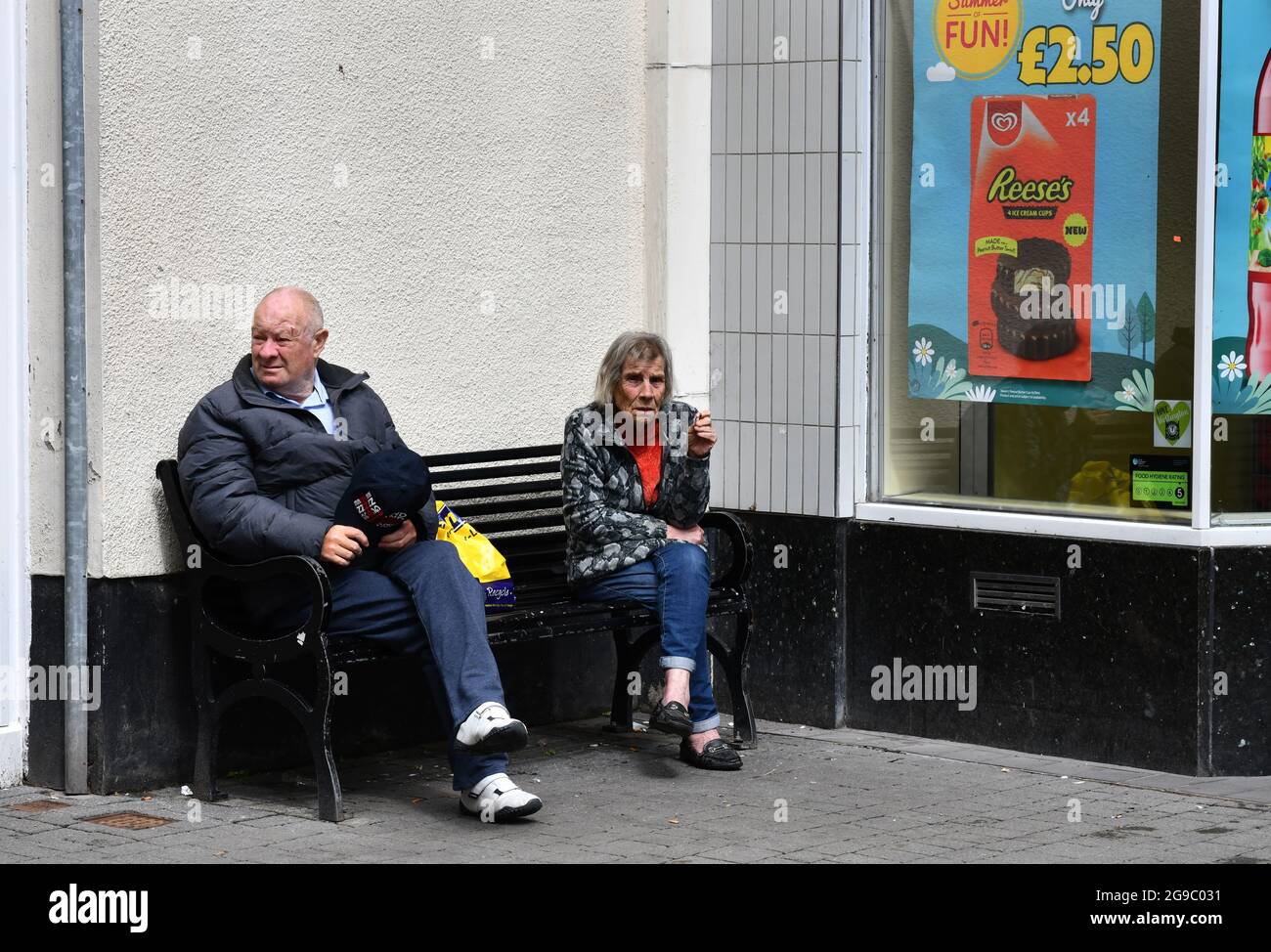 Elderly lady taking a seat while relaxing with a cigarette 2021. street streets Britain lifestyle smoking old seat bench town centre Uk Stock Photo