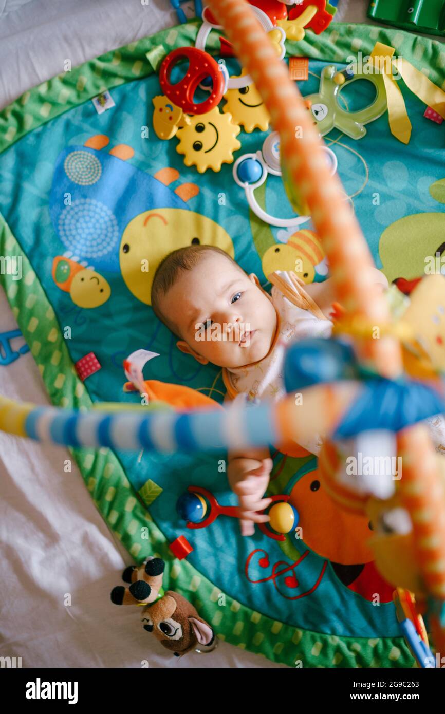 Baby lies on a play mat and reaches for the toys hanging above him Stock Photo