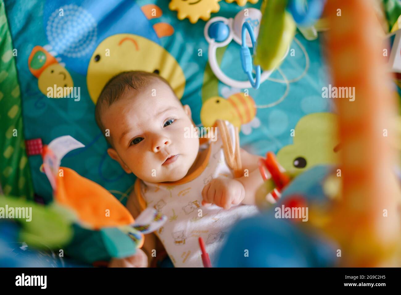 Baby lies on a play mat with toys hanging above him Stock Photo