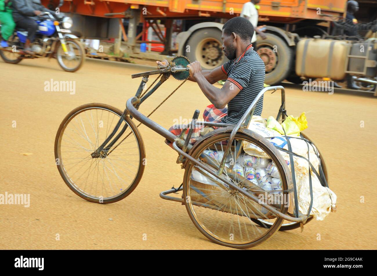 A man with a disability ridding a special designed wheel chair. The wheel chair is designed for transporting goods bought to Uganda from Kenya. The artisans came up with these designs to allow people with disability free movement and for daily living. Because of these specially designed wheel chairs people with disabilities can enjoy some of the same rights like other people. Uganda. Stock Photo