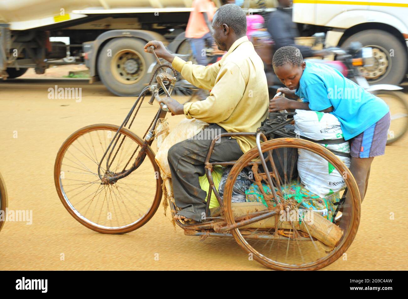 A man with a disability ridding a special designed wheel chair which his child. The wheel chair is designed for transporting goods bought to Uganda from Kenya. The artisans came up with these designs to allow people with disability free movement and for daily living. Because of these specially designed wheel chairs people with disabilities can enjoy some of the same rights like other people. Uganda. Stock Photo