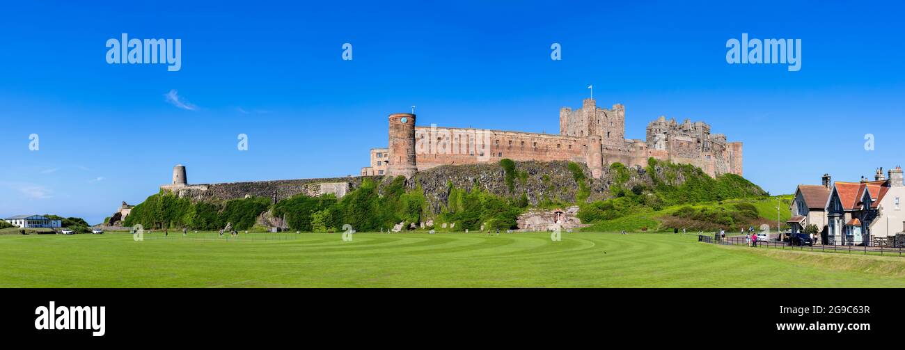 Iconic Bamburgh Castle and windmill by the cricket pitch in the coastal village of Bamburgh in Northumberland on the north-east coast of England Stock Photo