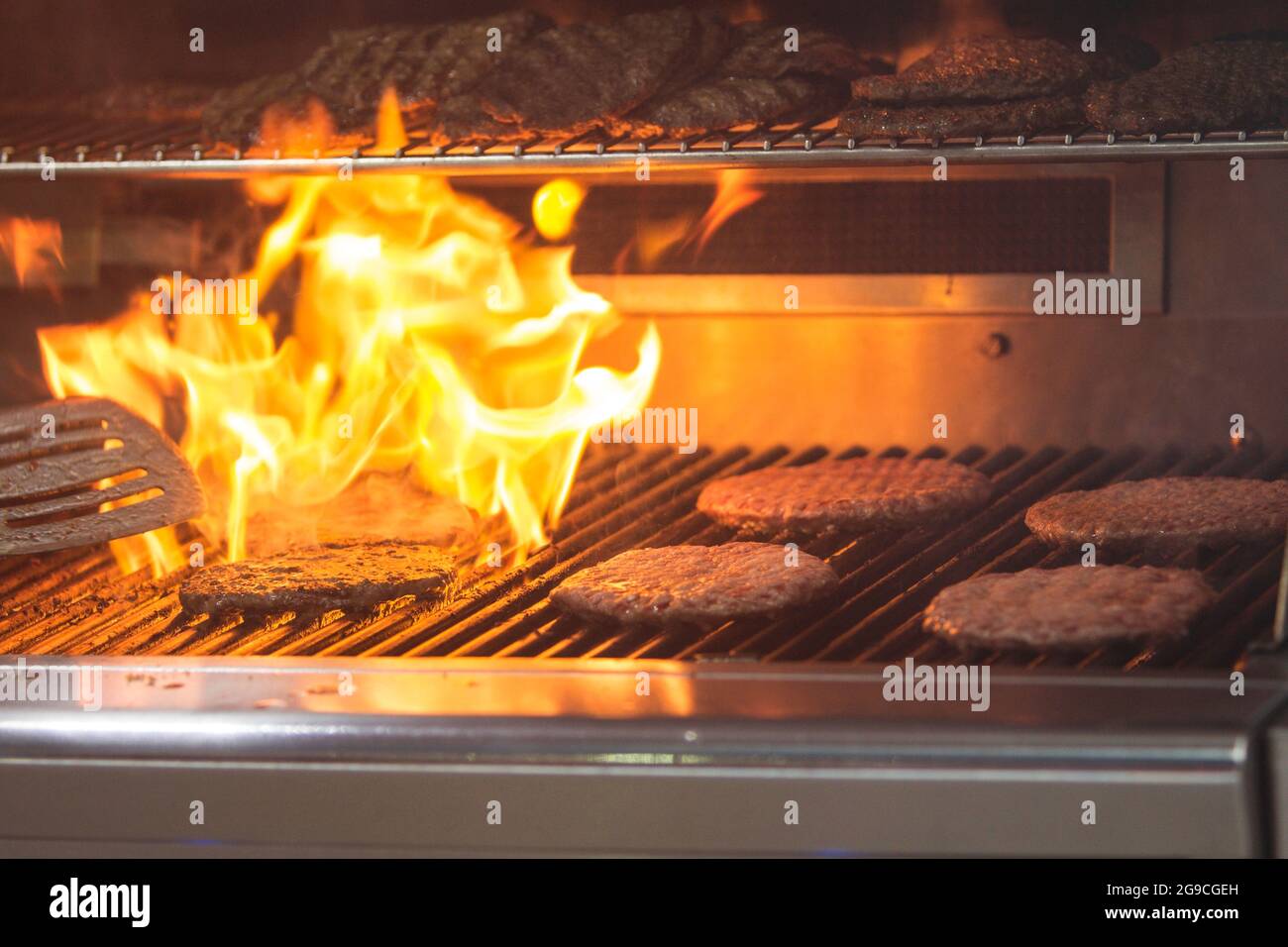 Hamburgers are charbroiled on a grill as flames shoot up through the