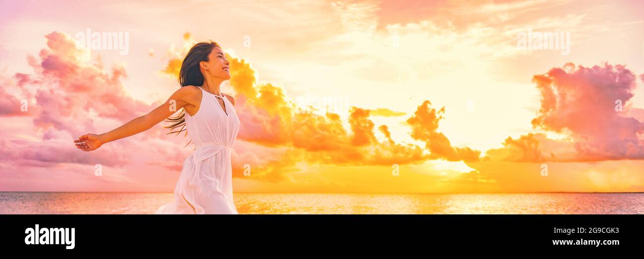 Well being free woman with open arms in the air blissful happiness concept banner. Happy woman against pink pastel colorful sunset sky Stock Photo