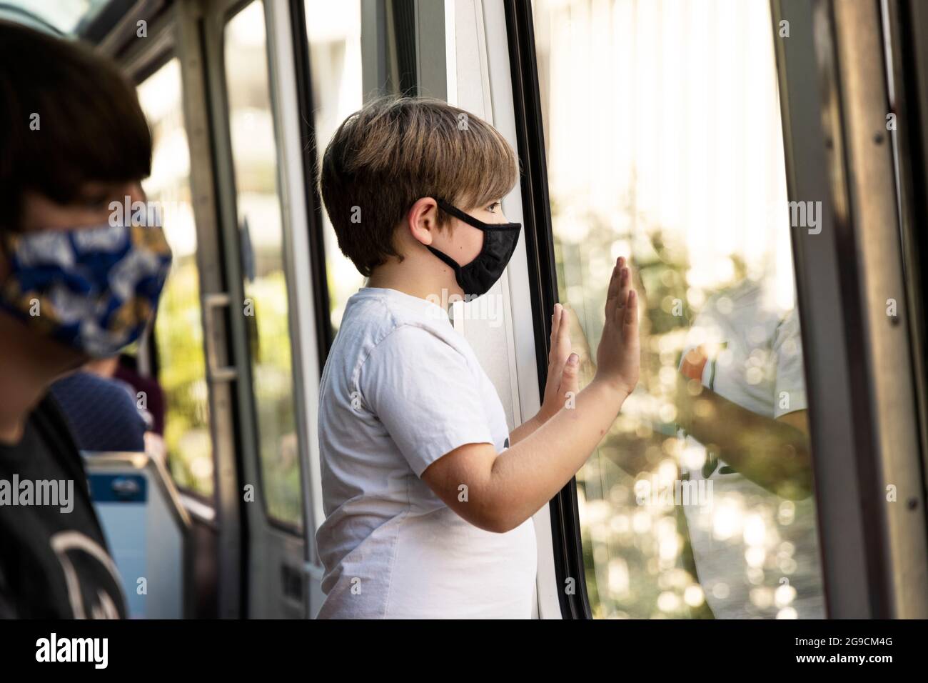 A boy wearing a face mask looks out the window while riding the