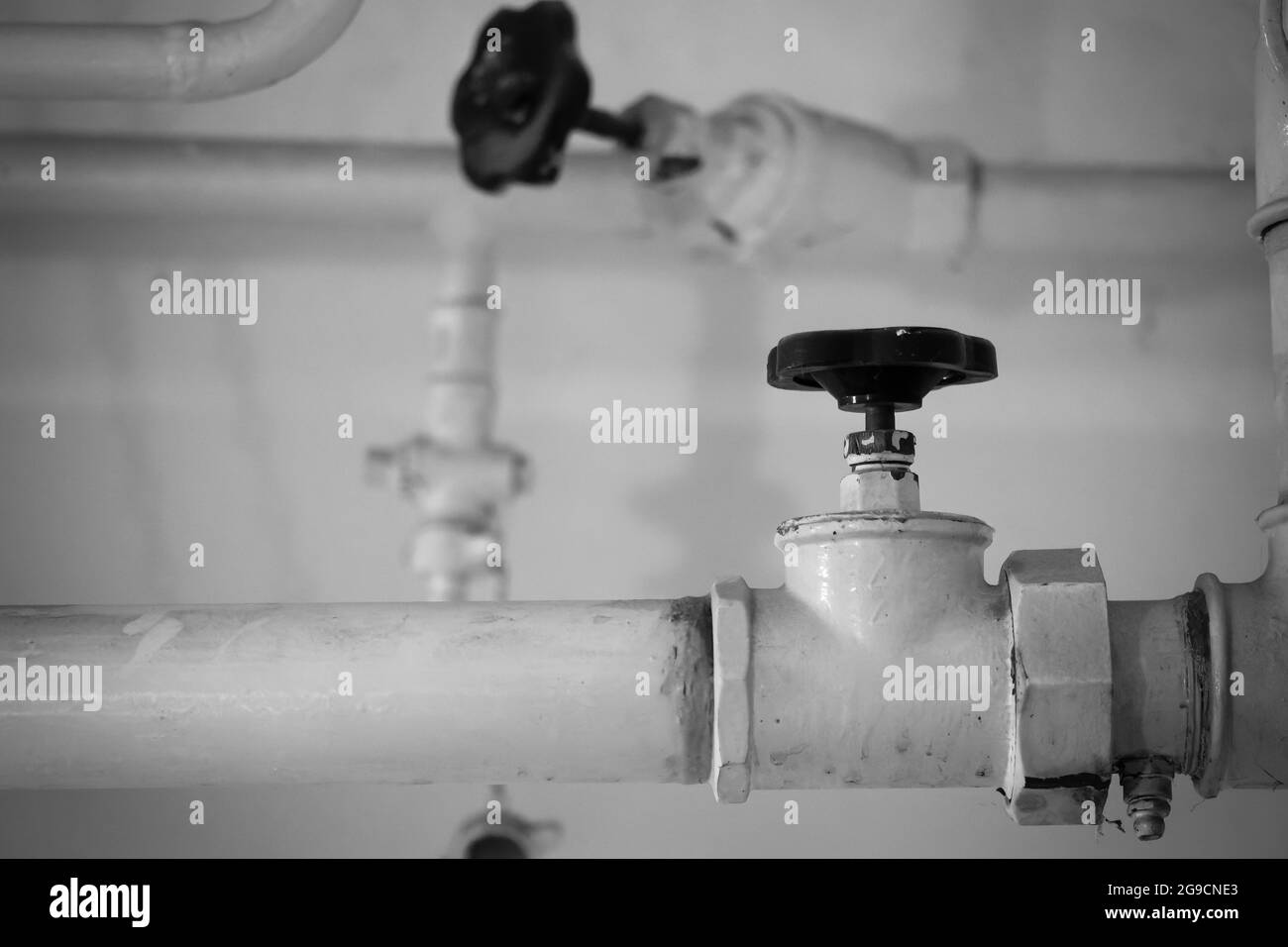 A grayscale closeup of two industrial water pipes indoors with a blurry