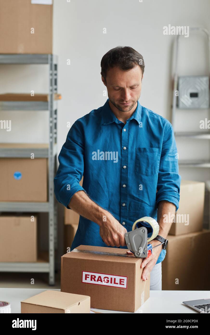Vertical portrait of young man packing boxes at warehouse with Fragile sticker, copy space Stock Photo