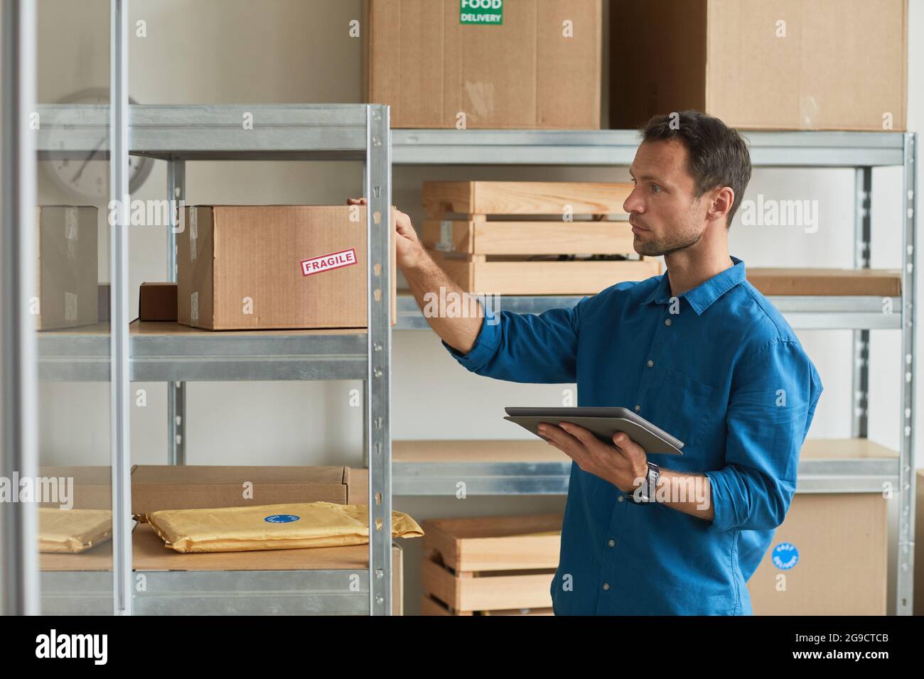 Side view portrait of young man using digital tablet in warehouse while doing inventory and managing small business, copy space Stock Photo